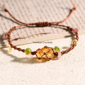 Handmade citrine gemstone cord bracelet with green and pink crystal accents on a textured light surface with paper background