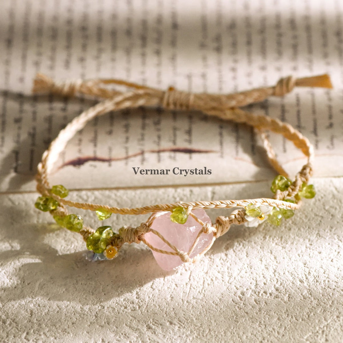 Handcrafted rose quartz double wrap braided bracelet with green beads on natural cord displayed on textured surface