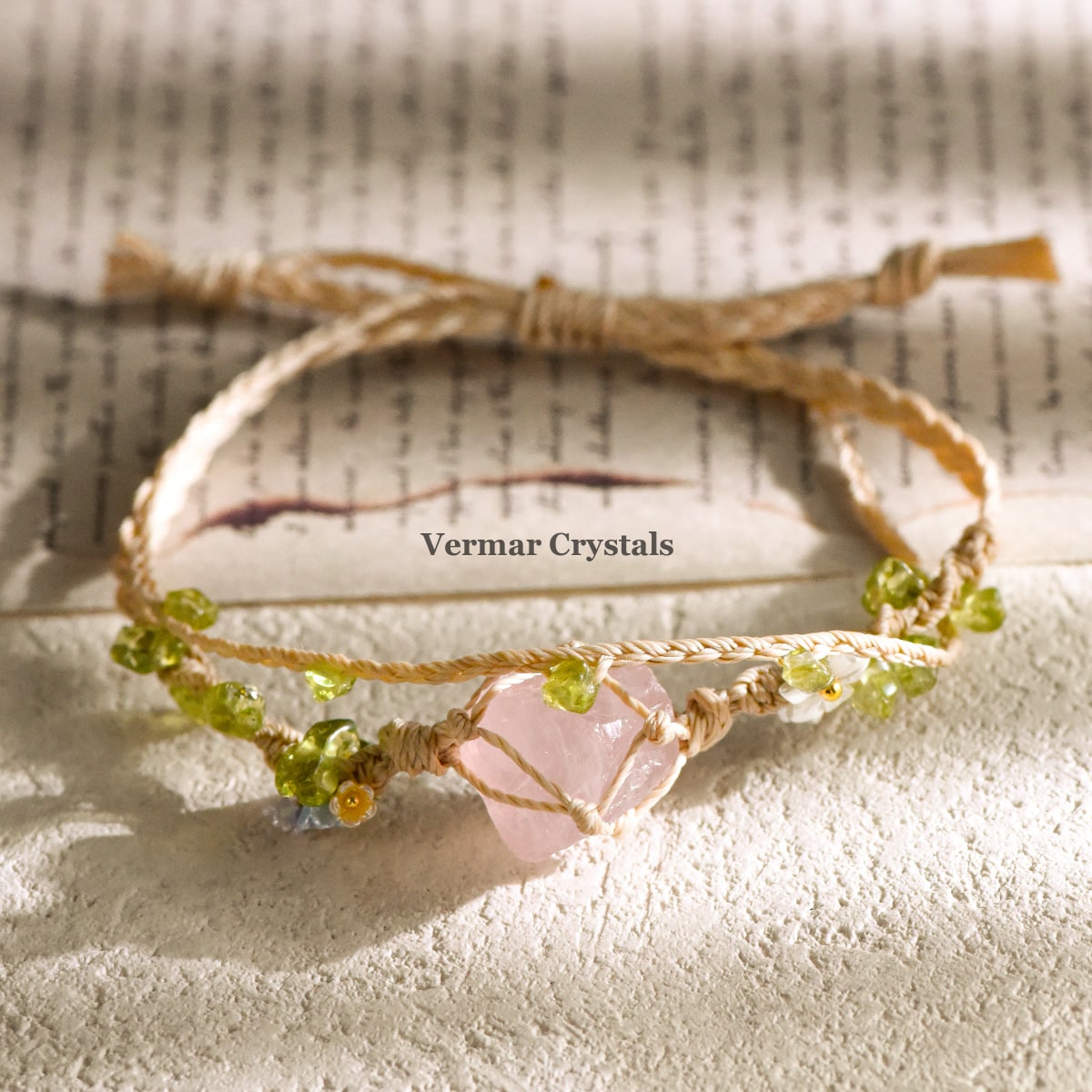 Handcrafted rose quartz double wrap braided bracelet with green beads on natural cord displayed on textured surface