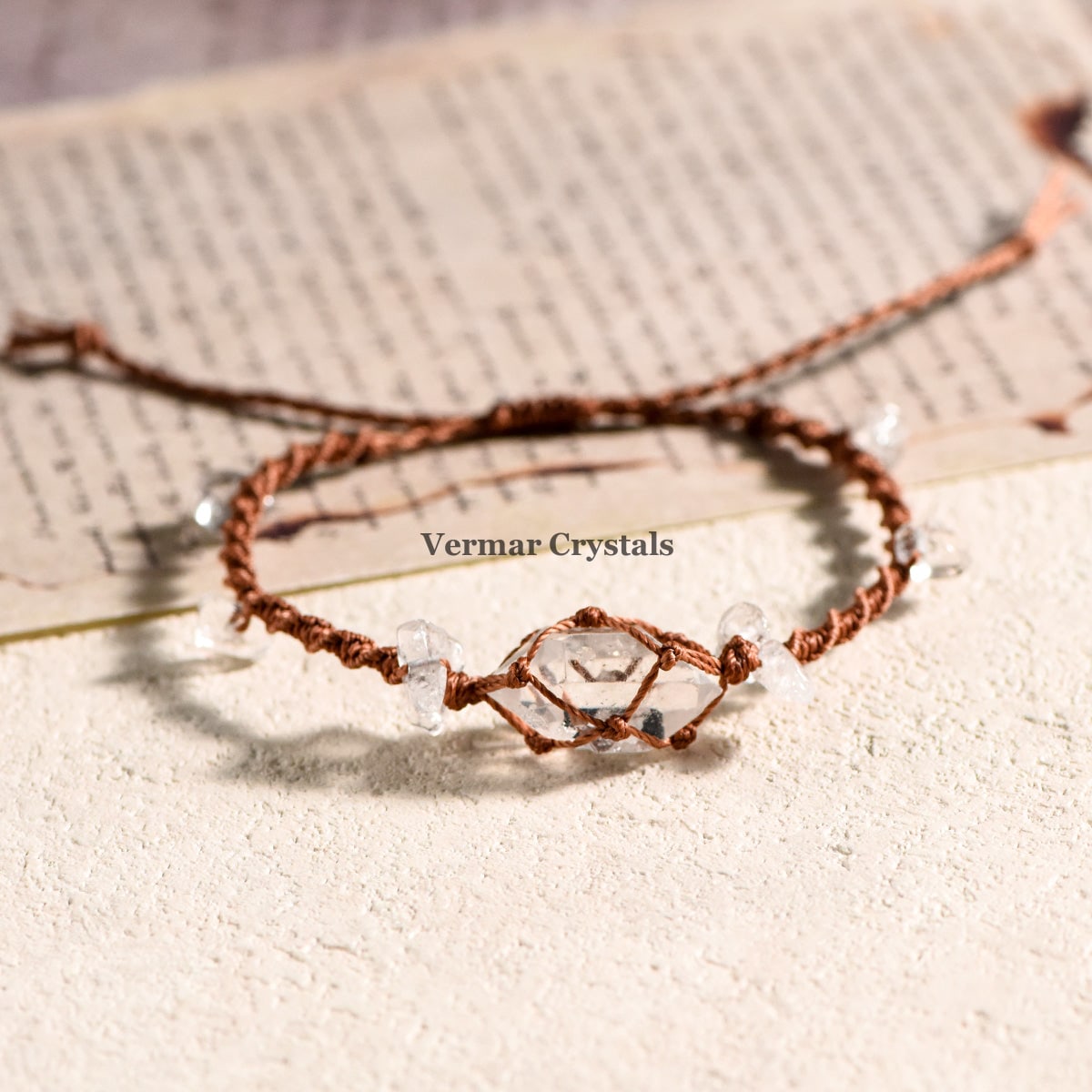 Handcrafted Herkimer Diamond bracelet with clear stones on braided brown cord resting on textured surface and paper background
