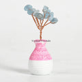 Small aquamarine crystal tree ornament with wire branches in a pink and white ceramic vase on white background