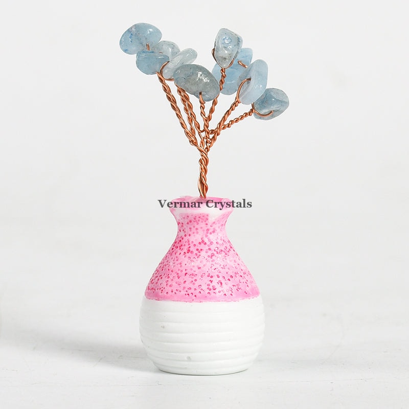 Small aquamarine crystal tree ornament with wire branches in a pink and white ceramic vase on white background