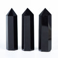 Three polished black obsidian crystal towers with smooth reflective surfaces on a white background