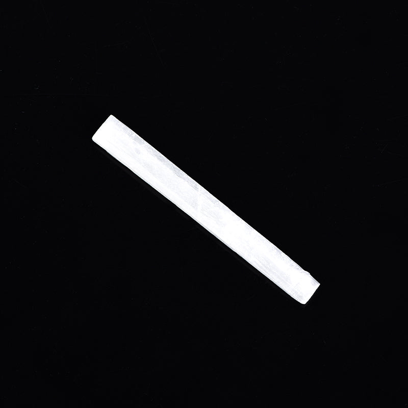 Natural 10cm selenite stick crystal next to a brown kraft paper tag on solid black background