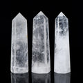 Three natural clear quartz crystal towers with polished pointed tips on a reflective black surface background