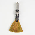 Handcrafted mini witch broom with natural straw, polished crystal point handle, and silver fairy charm on white background