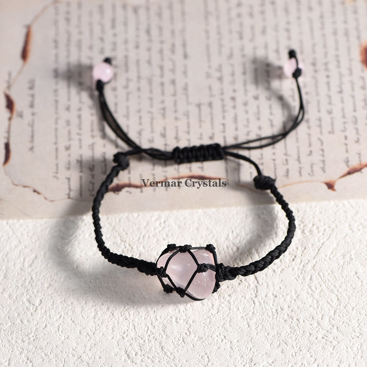 Handmade bracelet with a natural tumbled rose quartz stone wrapped in black macrame cord on a white surface