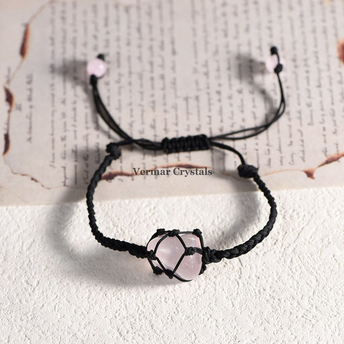 Handmade bracelet with a natural tumbled rose quartz stone wrapped in black macrame cord on a white surface