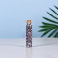 Mini glass vial filled with natural purple amethyst crystal chips sealed with cork on white surface and blue background