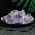 Pile of irregular transparent amethyst crystal stones with purple hues on a black dish against dark background