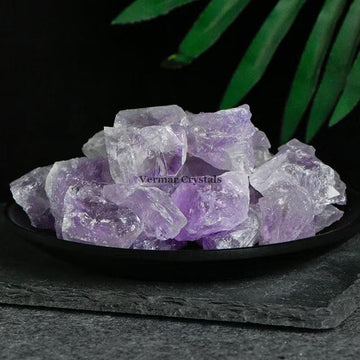 Pile of irregular transparent amethyst crystal stones with purple hues on a black dish against dark background