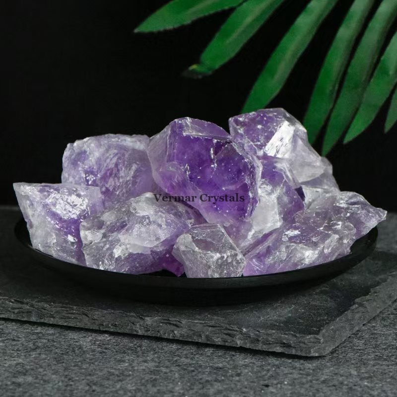 Pile of irregular transparent amethyst crystal stones with purple hues on a black dish against dark background