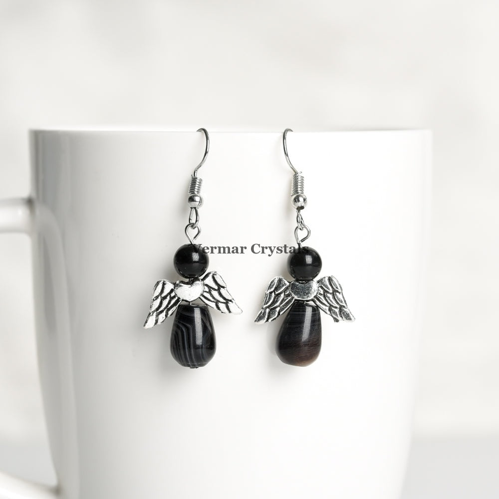 Pair of handcrafted black agate angel earrings with silver wings hanging from hooks on white cup background
