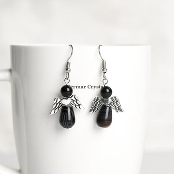 Pair of handcrafted black agate angel earrings with silver wings hanging from hooks on white cup background