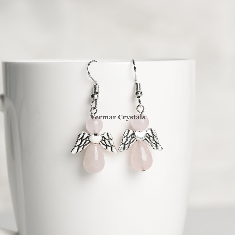 Delicate rose quartz angel earrings with silver wings and natural pink stones hanging on white ceramic cup