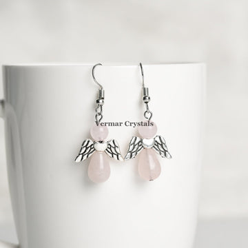 Delicate rose quartz angel earrings with silver wings and natural pink stones hanging on white ceramic cup