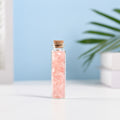 Mini glass vial filled with natural rose quartz crystal chips sealed with a cork against blue background
