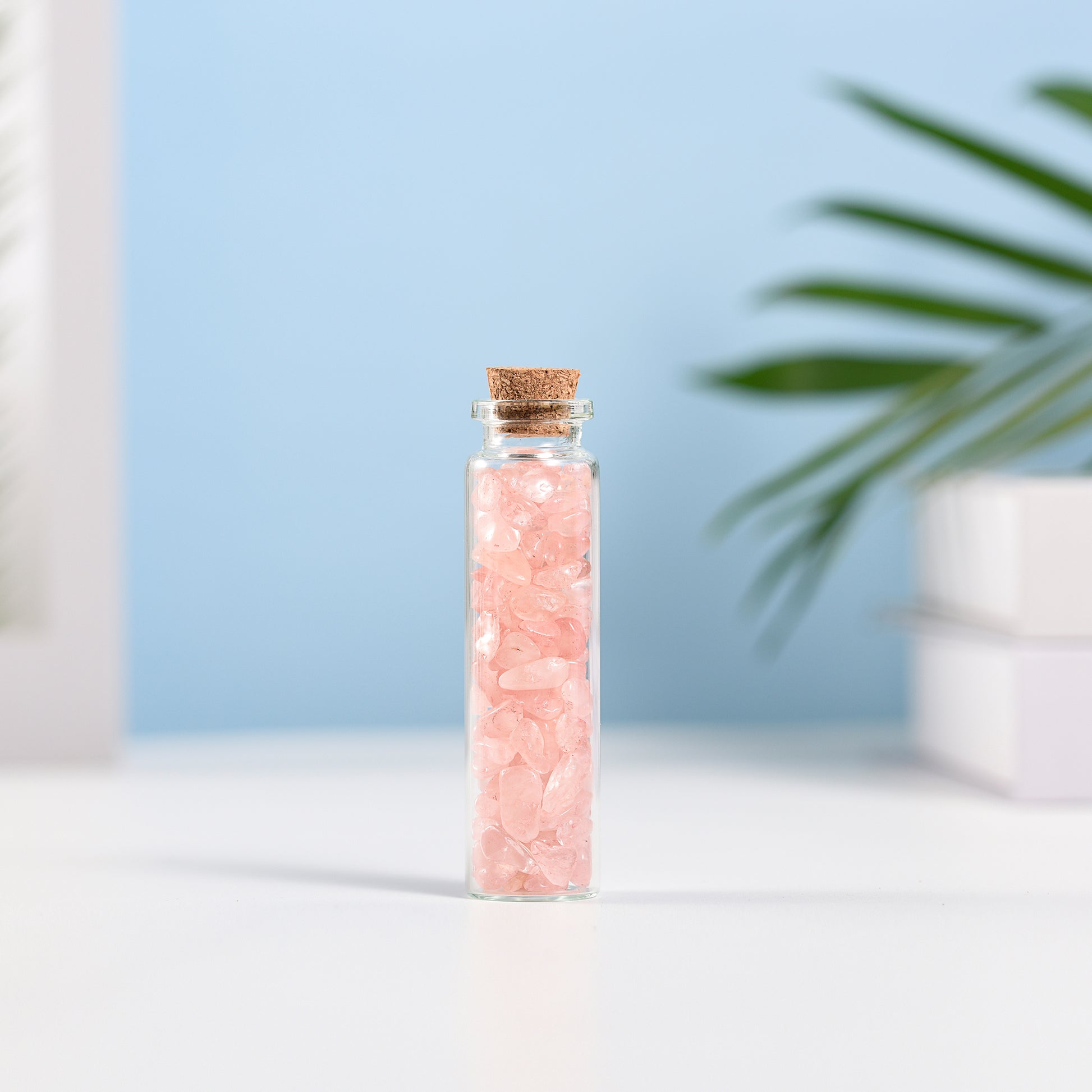 Mini glass vial filled with natural rose quartz crystal chips sealed with a cork against blue background