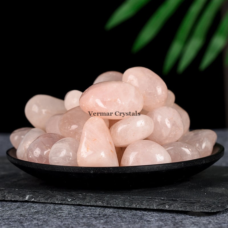 Pile of polished rose quartz tumblestones with soft pink hues displayed on a black plate against dark background