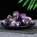 Black dish filled with smooth polished amethyst tumblestones in various shades of purple on a dark surface