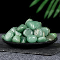 Polished green aventurine tumblestones arranged on a black dish with a dark background and green leaves above