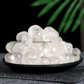 Pile of polished clear quartz tumblestones displayed on a black dish with a dark background and green leaf detail